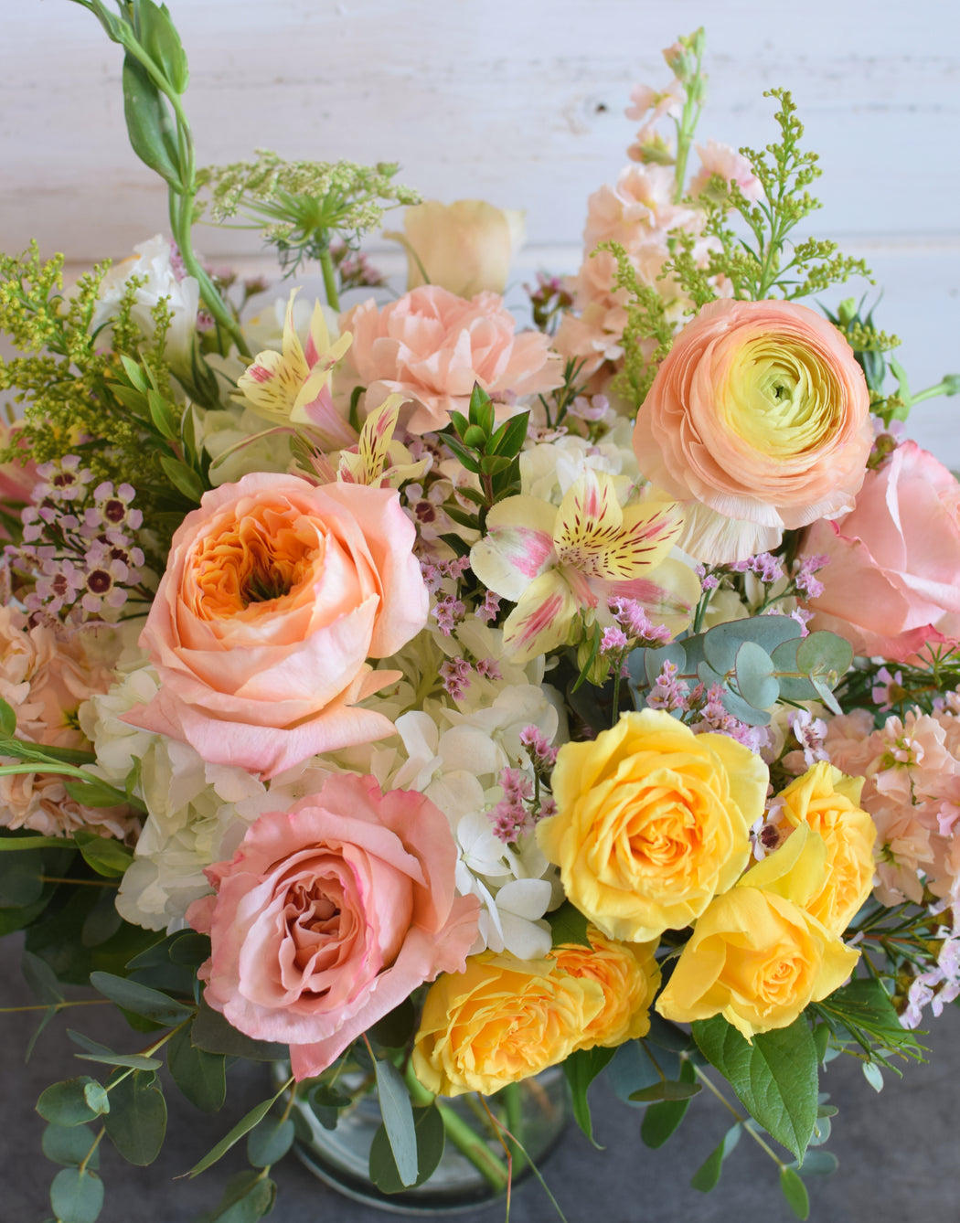 Close up view of the vibrant yellow roses  and white hydrangea center and delicate peach rose petals in the Creamsicle floral design.