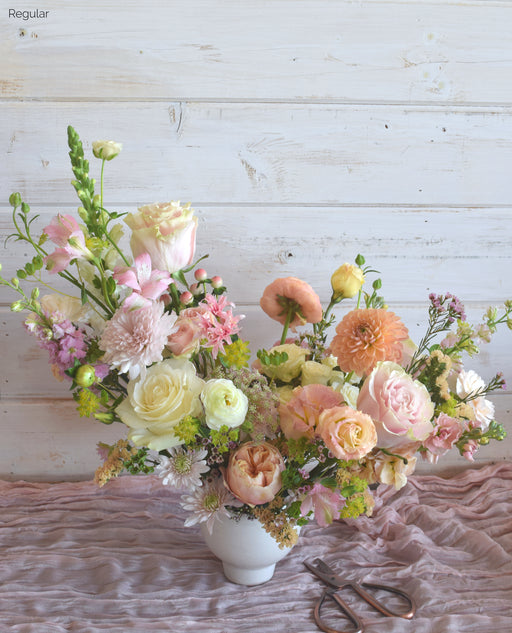 Pastel mixed flower arrangement named the Free Spirit featuring peach dahlias, blush garden roses, and white ranunculus in a modern low-profile bowl.