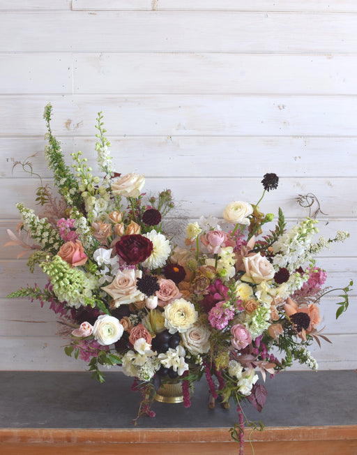 Huge, lush, and totally overflowing with premium blooms and greenery, this thing is by far the biggest arrangement on our menu. Designed in a mix of high-end vases, it’s a serious statement piece. Full Bloom bold colorway flower arrangement featuring fresh bold roses, dark dahlias, and burgundy ranunculus for local delivery in Laguna Woods CA.