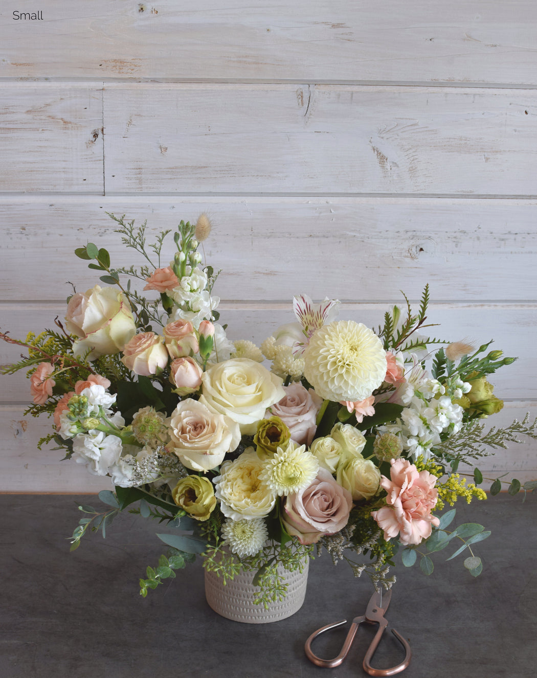 Neutral-colored roses, lisianthus, ranunculus, Queen Anne's lace, bunny tail, eucalyptus, dahlias, and peonies arranged in a contemporary clay vase, creating a fresh, nature-inspired floral bouquet.