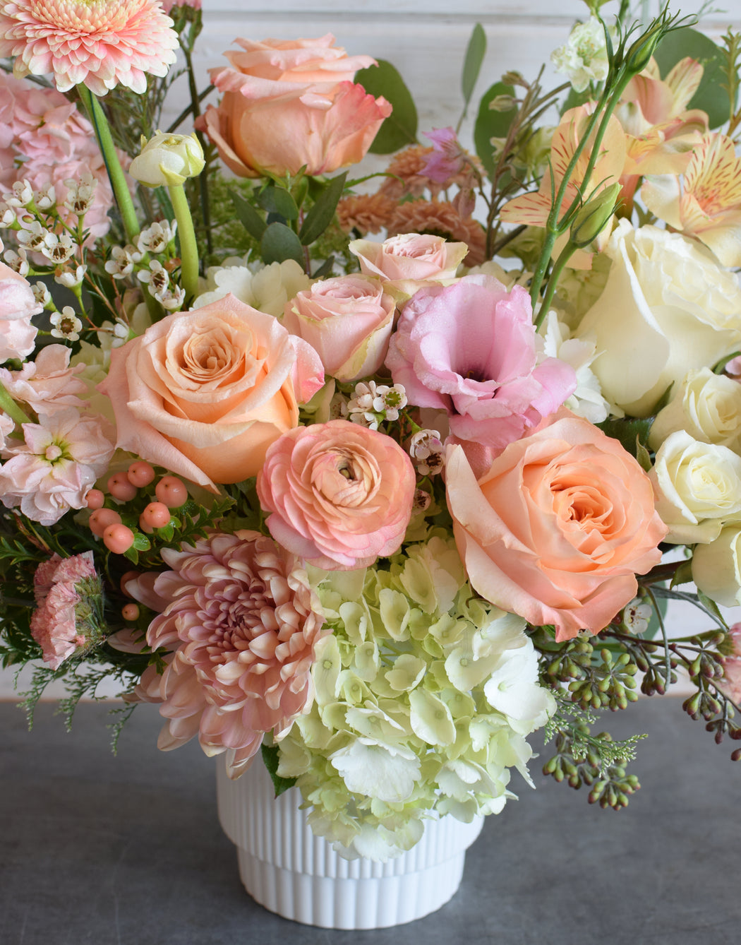 Bouquet of flowers with pink, orange, and white roses in a white vase.