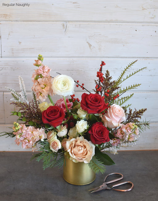 Festive Naughty version of Sleigh All Day flower arrangement by Flowerful, featuring bold red roses, ranunculus, spray roses, and pine in a gold vessel, perfect for Christmas in Orange County.