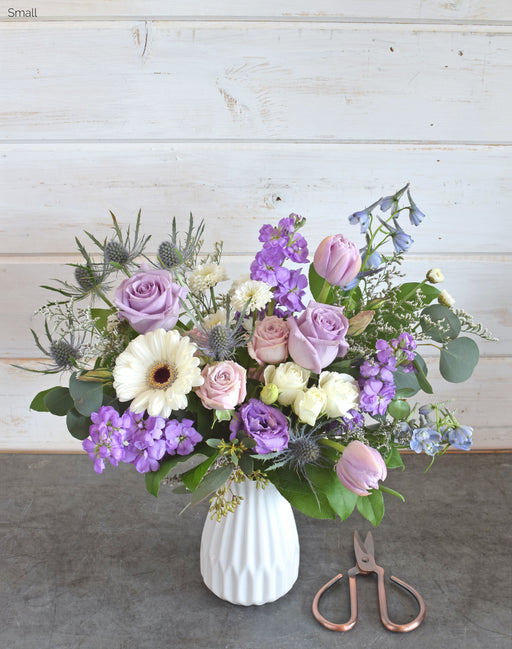 The Wild Berry flower arrangement, size small, with roses, tulips, lisianthus, blue delphinium, and eucalyptus in a white ceramic fluted vase.