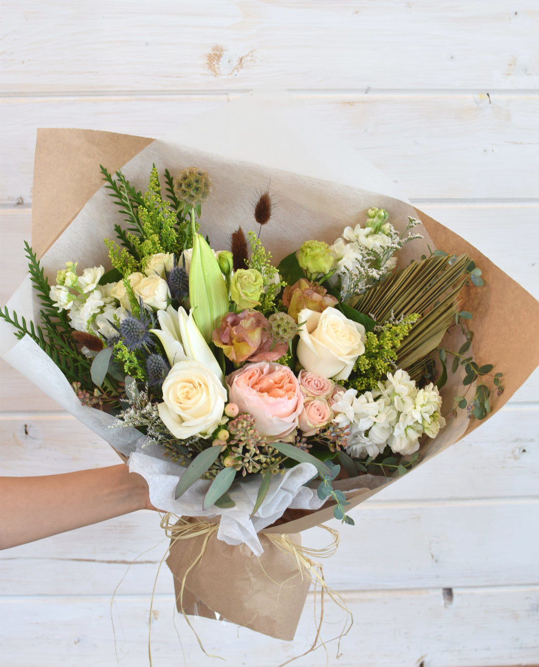 Neutral flower wrap with roses, eucalyptus, carnations, thistle, lilies, and more, wrapped in Kraft paper and tied with twine, creating a cozy, natural look for any occasion.